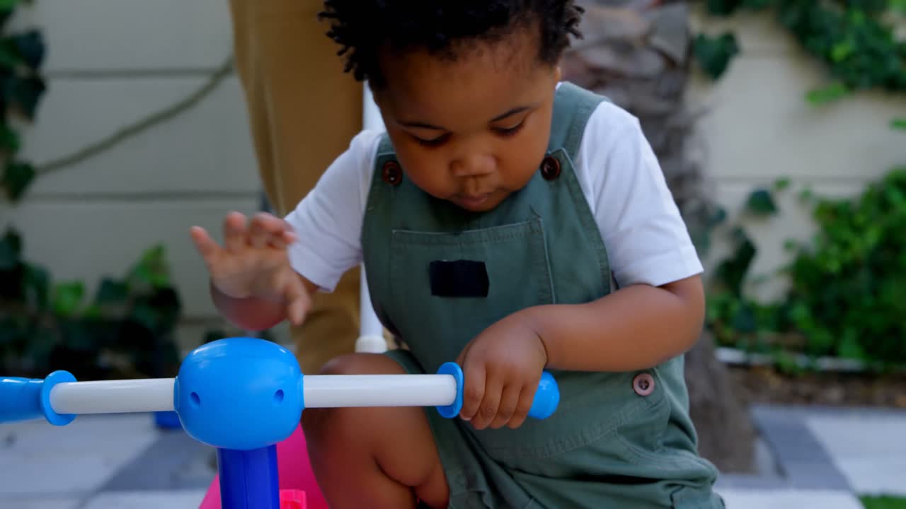 Close-up of cute little black boy playing with tricycle in back yard of their home 4k