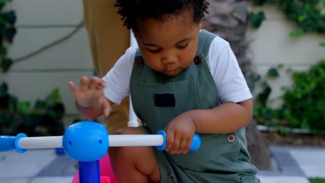 Close-up-of-cute-little-black-boy-playing-with-tricycle-in-back-yard-of-their-home-4k