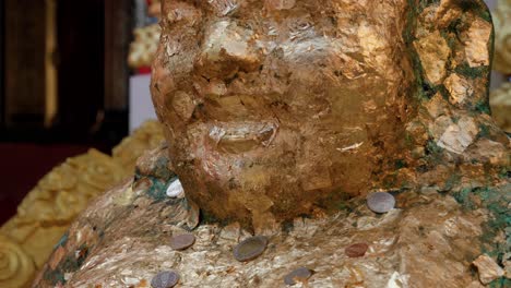 panning view of golden buddha statue covered with coins offered for good luck at buddhist temple, thailand