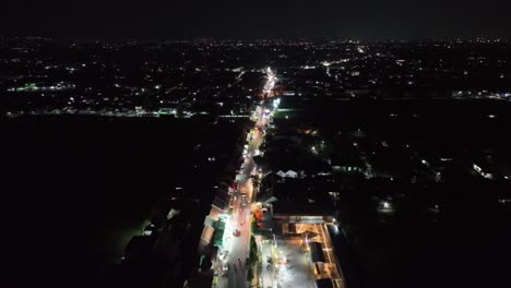 Nighttime-drone-flight-down-the-mainstreet-of-Wedi,-Klaten