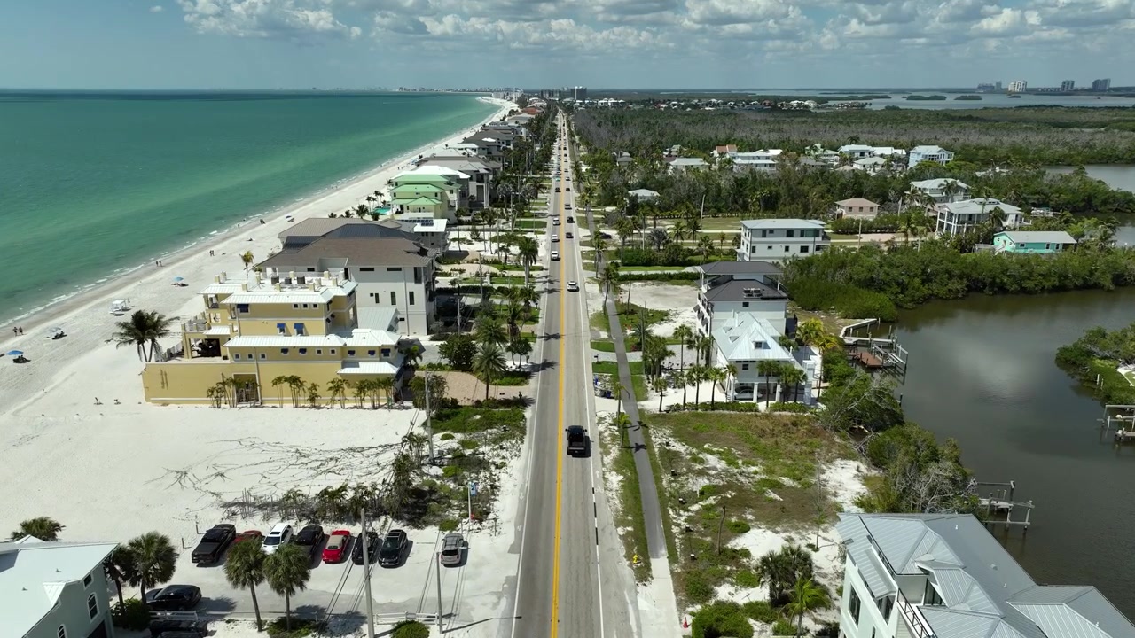 Flygfoto på låg höjd över Bonita Springs, Florida, som avslöjar kilometerlånga orörda stränder, kristallklart gulfvatten, palmkantade gator och lyxiga fastigheter vid kusten