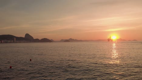 Low-aerial-approach-over-water-of-an-oil-platform-outside-of-the-Rio-de-Janeiro-coastline-in-Copacabana-with-the-Sugarloaf-mountain-on-the-left