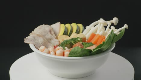 close up of a bowl of shabu ingredients spinning around on white table in the black background kitchen