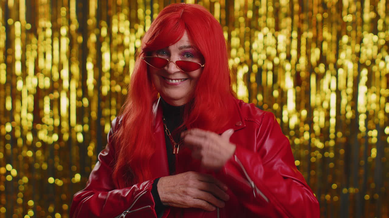 선글라스를 착용 한 즐거운 여성은 눈을 이고 미소로 카메라를 보고, 눈 이고, 유혹합니다.