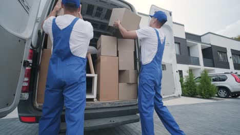 dos jóvenes trabajadores de una compañía de mudanzas están cargando cajas y muebles en un minibus