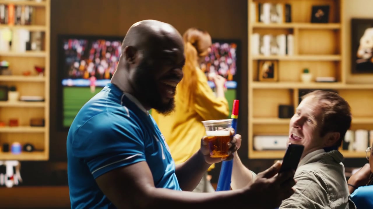 Uomo sul divano con il telefono in mano che racconta agli amici il risultato negativo della partita di calcio.