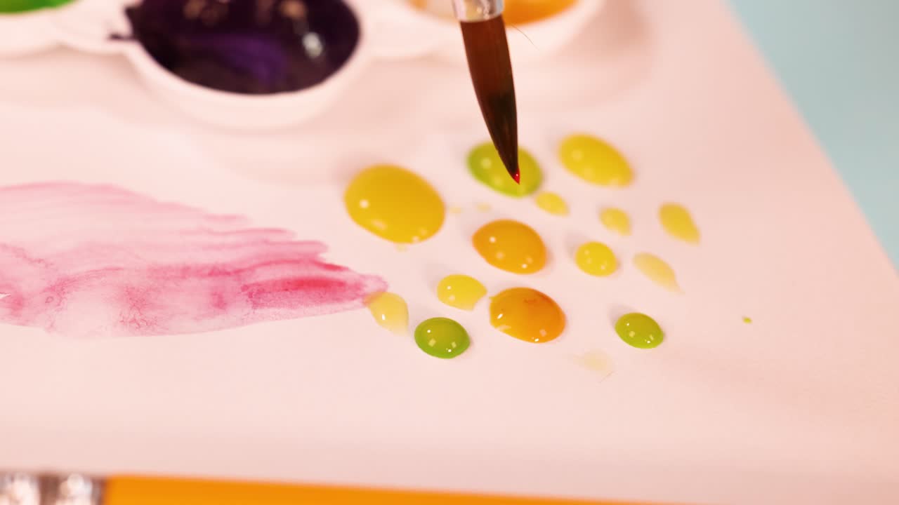 Artist uses round brush to paint yellow and green watercolor dots on white paper palette