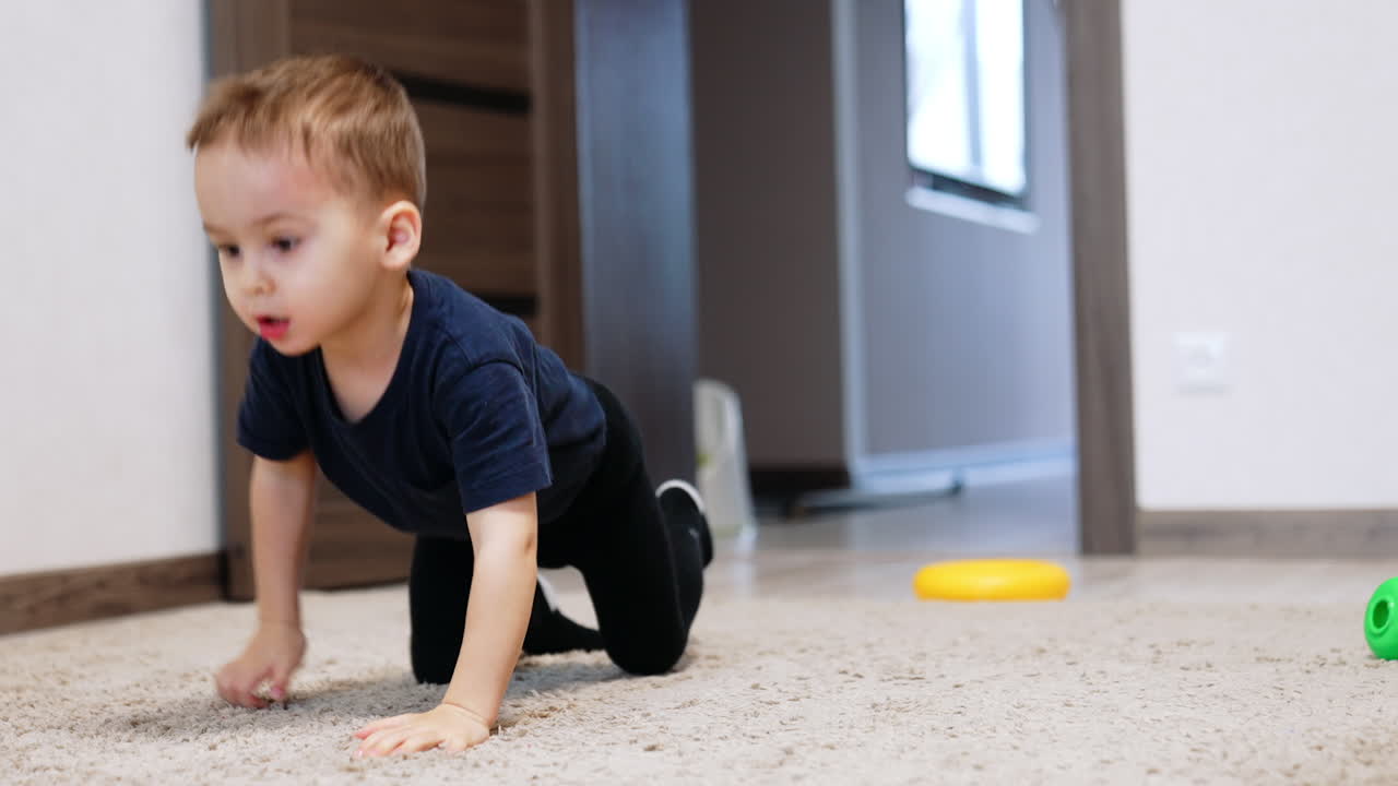 Active toddler boy crawling by the carpet. Smiling cute kid playing a game at home.