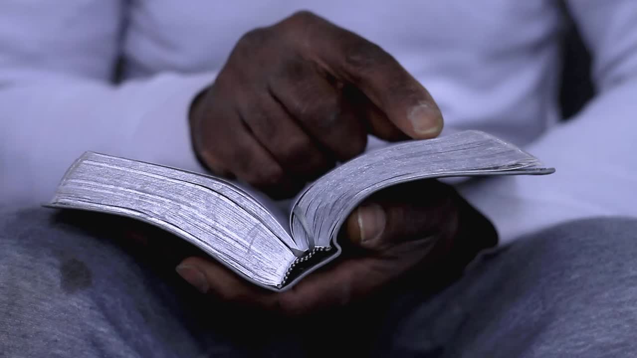 man praying to god with hands together with bible Caribbean man praying with white background stock footage