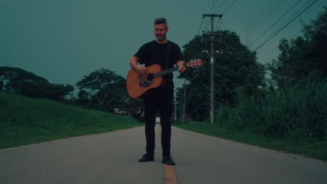man playing acoustic guitar on a country road at twilight
