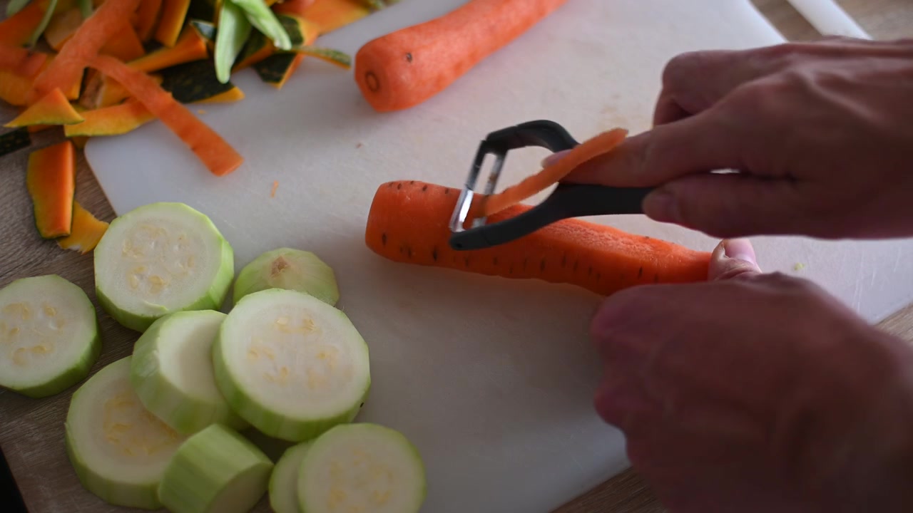Skalar färsk morot i köket med en grönsaksskalare.