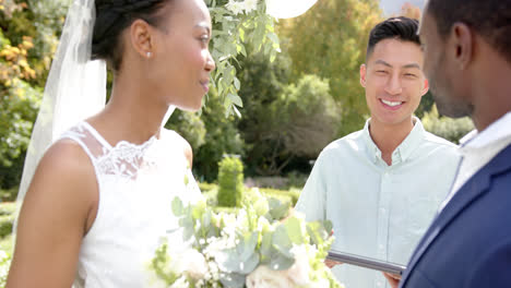 Hombre-Birracial-Oficiando-El-Matrimonio-De-Una-Feliz-Pareja-Afroamericana-En-Un-Jardín-Soleado,-En-Cámara-Lenta