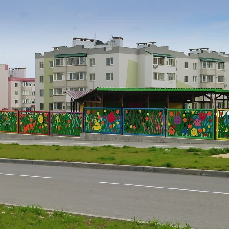 Valla colorida, bonita y encantadora del recinto de una guardería. Modernos bloques de apartamentos al fondo.