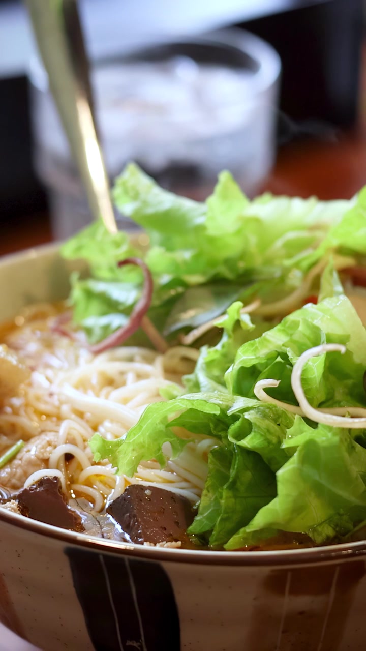 Un primo piano di zuppa di noodle vietnamita fumante guarnita con foglie fresche di lattuga verde