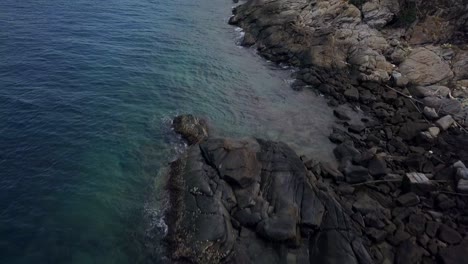 Aerial:-A-slow-forward-flight-over-the-rocky-shore-and-big-stones-revealing-the-horizon,-island-and-mountains-in-the-dsitance,-Thailand