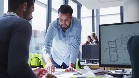 Two-diverse-male-colleagues-looking-at-architectural-blueprints-on-a-desk-and-talking