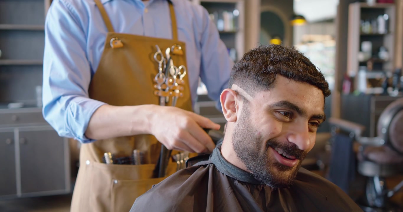 Frisør tænder klippemaskine, klipper mandlig kunde i barbershop, bruger kam, former skarp fade.