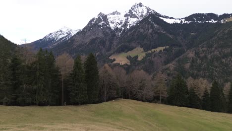 Drone-fly-next-to-summit-cross-towards-forest-with-snow-capped-winter-mountain-landscape-in-Austria