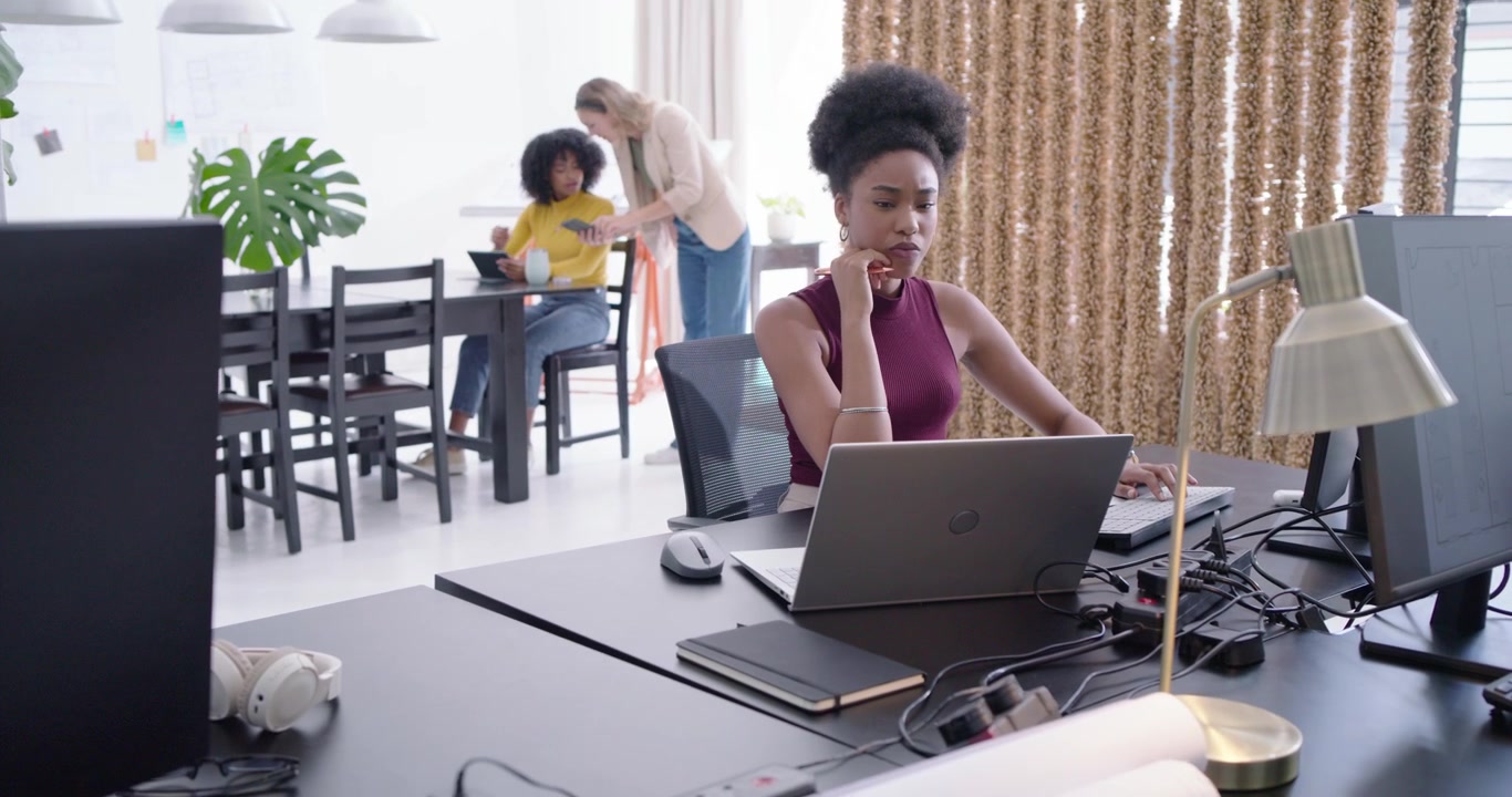 Et mangfoldigt kvindeteam i et studie; kvinden forrest skriver på en bærbar computer og kigger op, mens en kollega peger på en tablet i forbindelse med arbejdet.