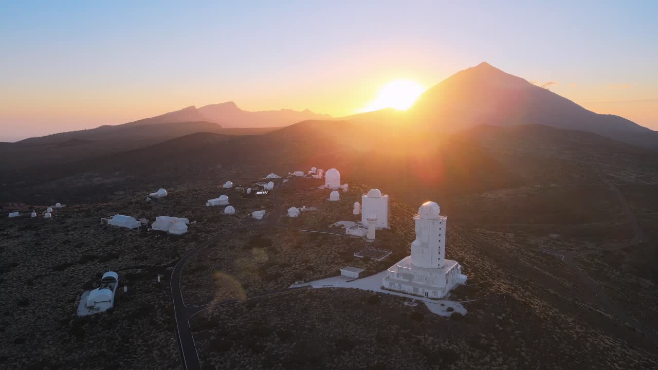 impresionantes tomas aéreas en círculos alrededor de observatorios blancos en montañas en tenerife españa, puesta de sol en segundo plano