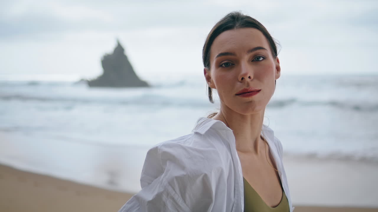 Ragazza in posa su una spiaggia cupa che si tocca i capelli, primo piano. Donna in piedi sulla riva del mare, scatto verticale.