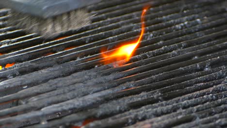 a wire brush cleans a grill as a small flame burns on some old food