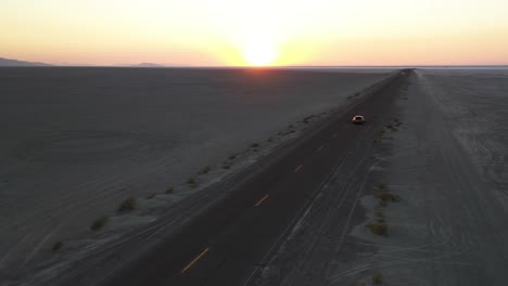 Luftaufnahme-Des-Autos,-Das-Auf-Der-Geraden-Wüstenstraße-Mit-Sonnenaufgangssonne-über-Dem-Tal-Fährt