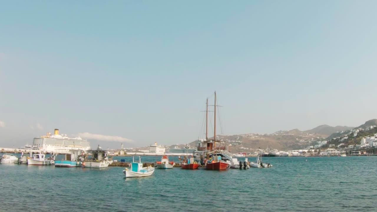 Barche ormeggiate in un porto a Mykonos mentre una nave da crociera arriva in lontananza