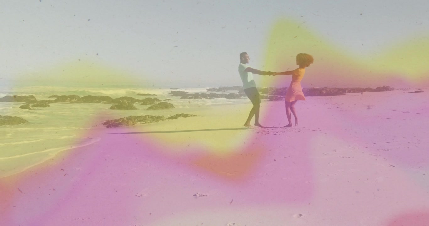 Donna che si avvicina a un uomo che la tiene e la fa girare sulla spiaggia, con un'atmosfera di viaggio romantico, sovrapposizione di colori rosa e giallo, e una coppia in un movimento ampio.