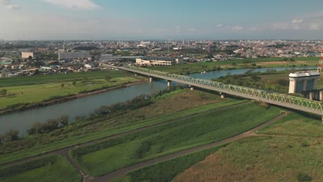 Ciudad-De-Fujimi-Desde-El-Río-Arakawa-Con-Un-Puente-Ferroviario-Y-Exuberantes-Campos-Verdes-En-Saitama,-Japón