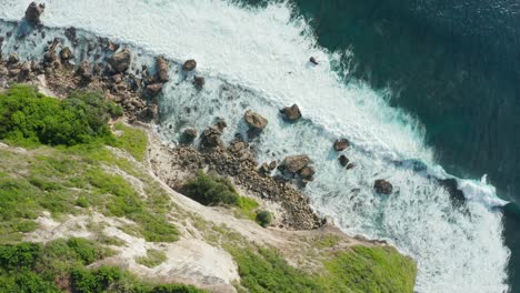 Aerial-top-down-view-of-a-rocky-coastline-with-white-foamy-waves-crashing-into-the-shore