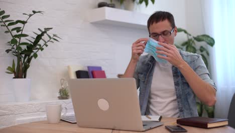 hombre tratando de quitarse la máscara de protección y trabajando en la computadora portátil