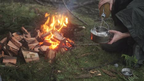 filling a kettle with water next to a bushcraft bonfire in the forest