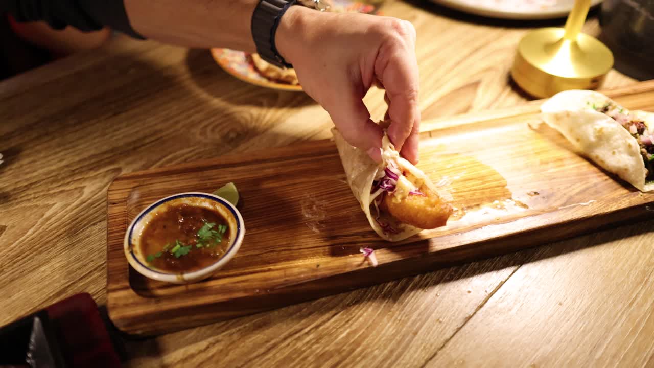 A person prepares and enjoys a taco at a warmly lit Mexican restaurant, highlighting the vibrant ingredients and inviting atmosphere