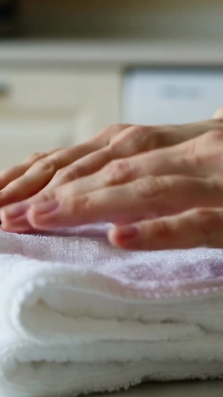 Vertikales Video: Eine rechte Hand tritt ein, Hände heben und glätten ein weißes Handtuch auf einer Theke.