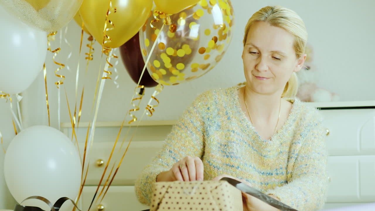 mamá envuelve una caja con un regalo en papel de envolver sentada junto a la cama en la habitación de los niños decorada con