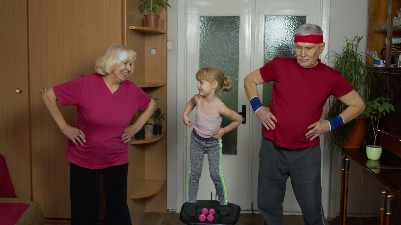 손녀와 성숙한 할아버지와 할머니는 스포츠 의상을 입고 스포츠 조을 하고 집에서 운동을 합니다.