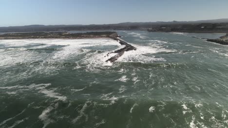 pulling back as ocean waves crash on the narrow coquille river jetty, oregon, aerial