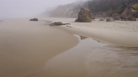 rainy day on oregon coast. low proximity drone flight over wet sand and rocks covered by fog. mystical dolly in aerial
