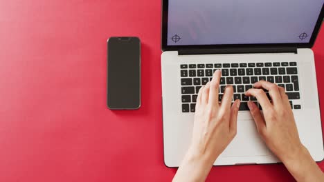 hands using laptop with smartphone on red desk with copy space