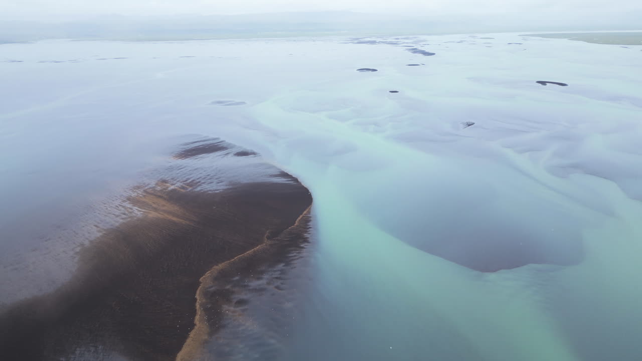 Aerial top down of River braids or Glacial River in different colors on Iceland island. Tilt up shot. Ocean seascape on background. Sunny summer day