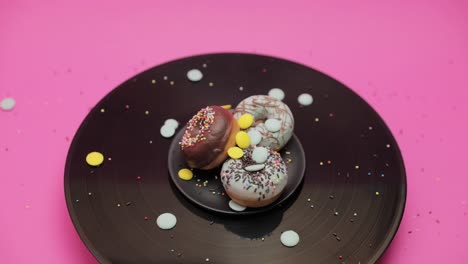 two blue chocolate american donuts and one chocolate  donut roll together in a circle on a black and pink surface