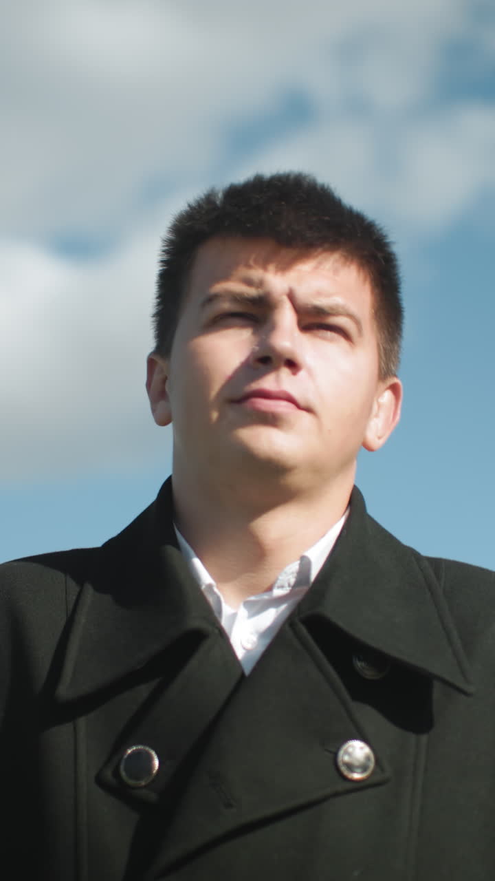 검은 코트를 입은 은행가는 빛이 반사되는 밖에서 자신감 있게 고 밝은 하늘 아래 도시 환경에서 흐릿한 거리 조명 기둥과 건물을 배경으로합니다.