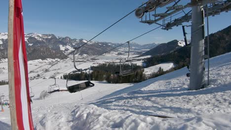 Toma-Panorámica-De-Un-Remonte-Que-Se-Mueve-Cuesta-Arriba-Con-Esquiadores,-En-El-Fondo-Un-Panorama-De-Un-Valle-Nevado-Y-Picos-Montañosos