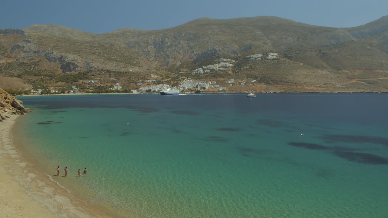plano general de una hermosa playa de arena y mar turquesa en una bahía paradisíaca, algunos nadadores se están bañando, egliali grecia, islas cícladas