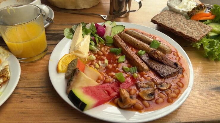 Plato de desayuno inglés tradicional con salchichas, frijoles, fruta y ensalada sobre la mesa