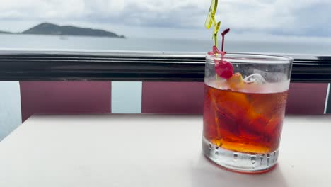 a negroni cocktail sits on a table overlooking the ocean, capturing a serene and picturesque moment at a cliffside restaurant