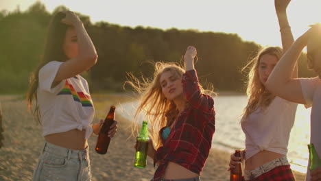 teenagers celebrate a birthday on the beach party with beer and good mood. they clink beer and dance in the hot evening. this is carefree party at sunset.