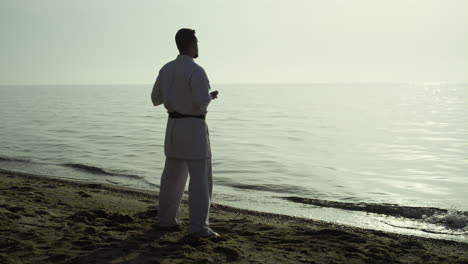 Deportista-Tranquilo-Entrenando-Karate-Viendo-La-Puesta-De-Sol-En-La-Playa.-Hombre-Haciendo-Ejercicio-Al-Aire-Libre.