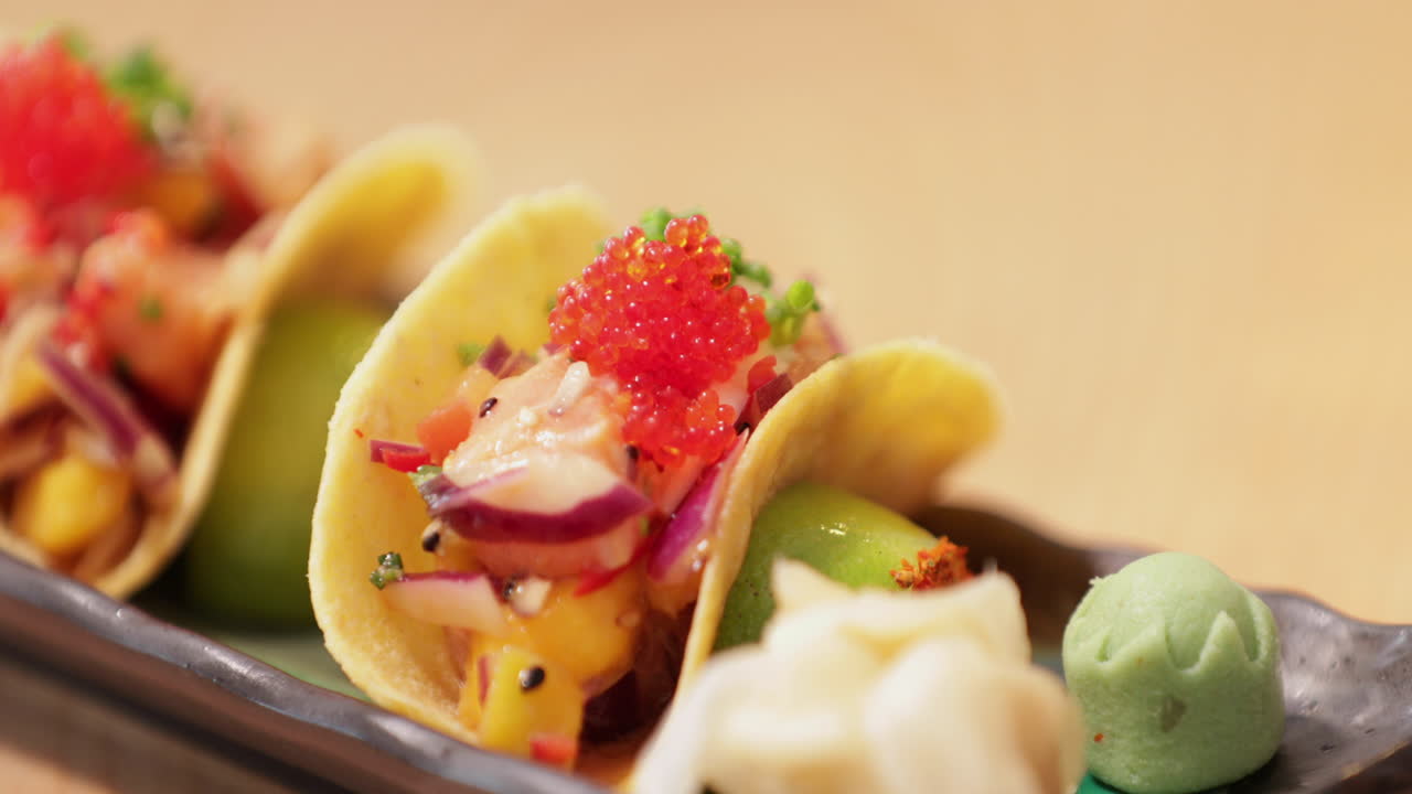 Añadiendo wasabi a un plato de tacos preparados cubiertos con caviar en un restaurante de sushi - primer plano.